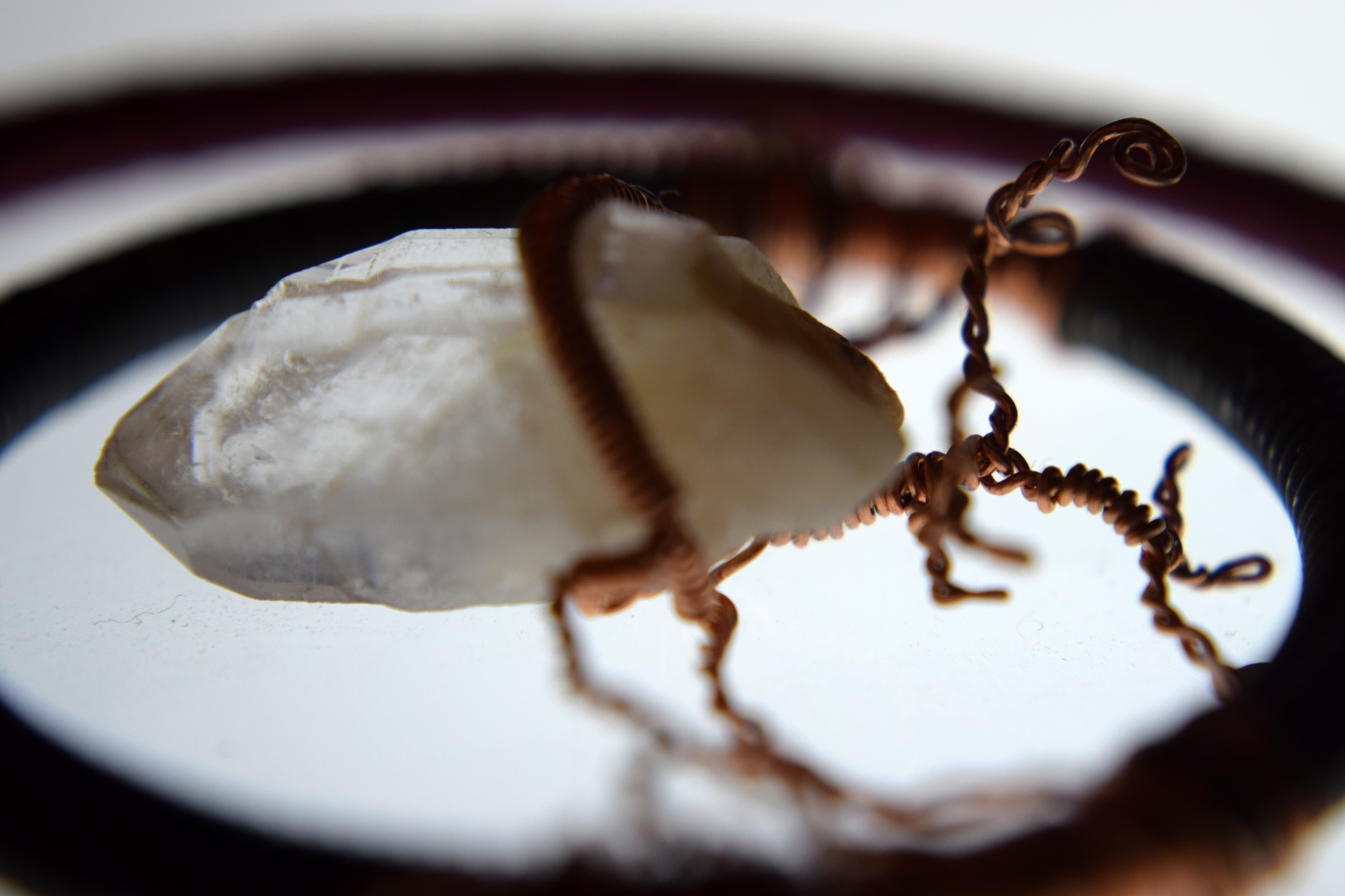 A quartz crystal wrapped in copper wire, suspended in a brass ring wrapped in steel wire